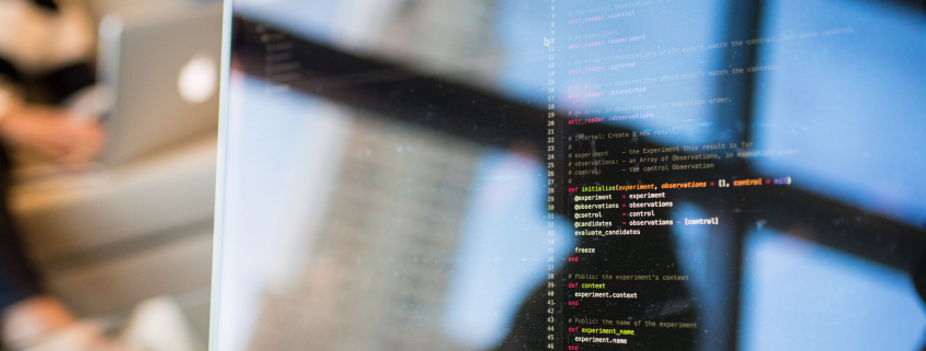 Close-up of a laptop screen showing lines of code in a text editor with colorful syntax highlighting, blurred background.